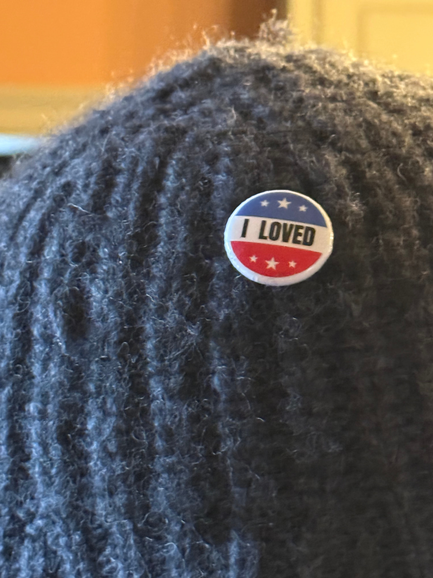 The small round red, white and blue I LOVED pin worn on the side of a dark grey knit beanie